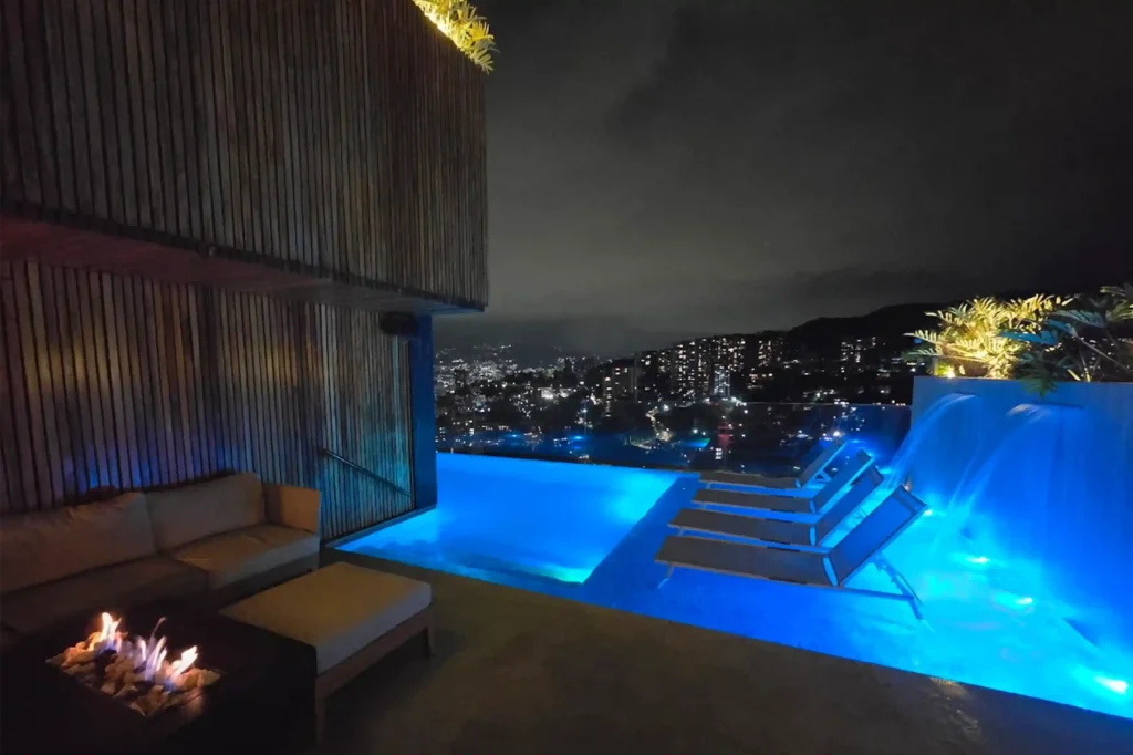 Piscina infinita iluminada de noche en el rooftop etro de BINN Hotel en Medellín con fogata lounge y vistas a las luces de la ciudad.