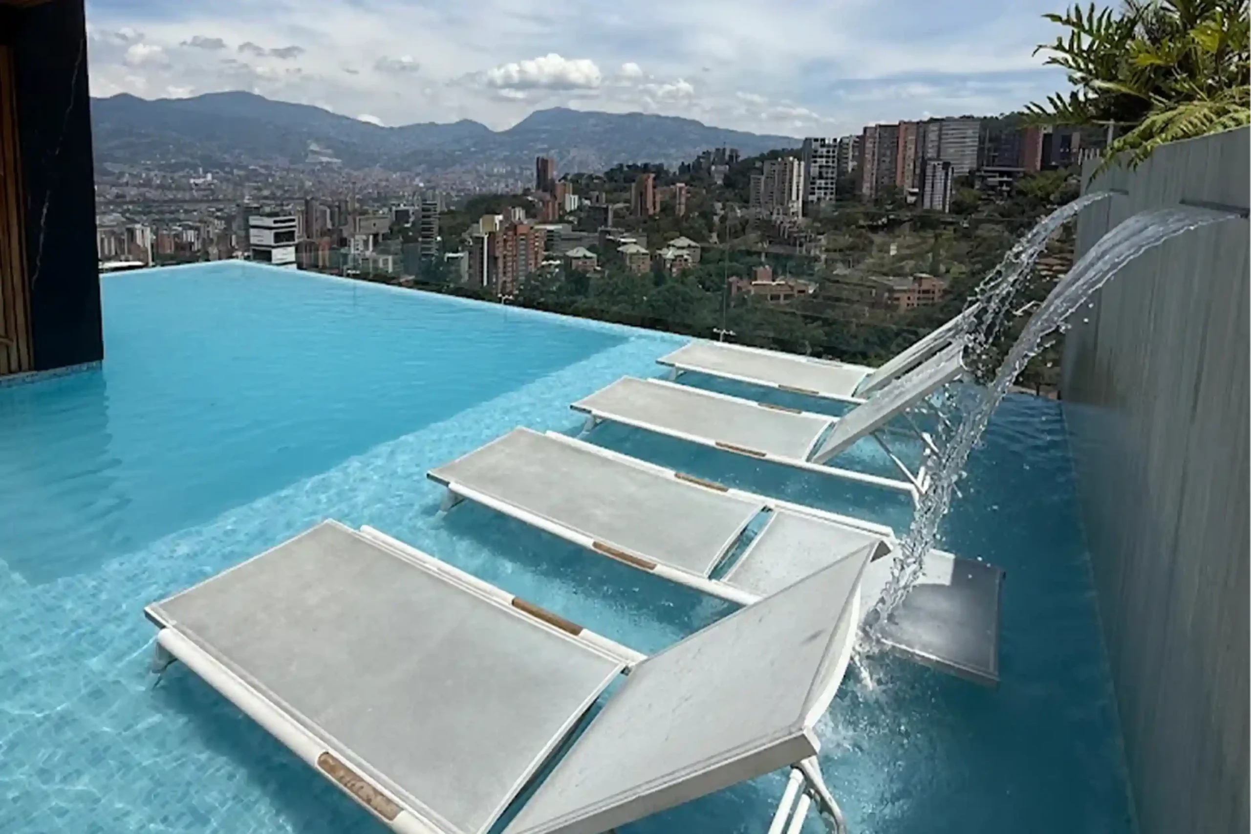Piscina infinita en rooftop de BINN Hotel en un de Medellín con tumbonas en el agua, cascadas decorativas y vista panorámica a la ciudad.