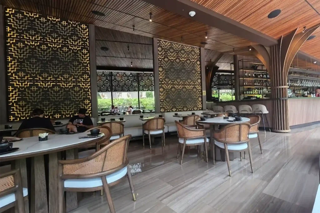 Restaurante de lujo La Makha de BINN Hotel en Medellín con paneles decorativos dorados, techos de madera y sillas de mimbre.
