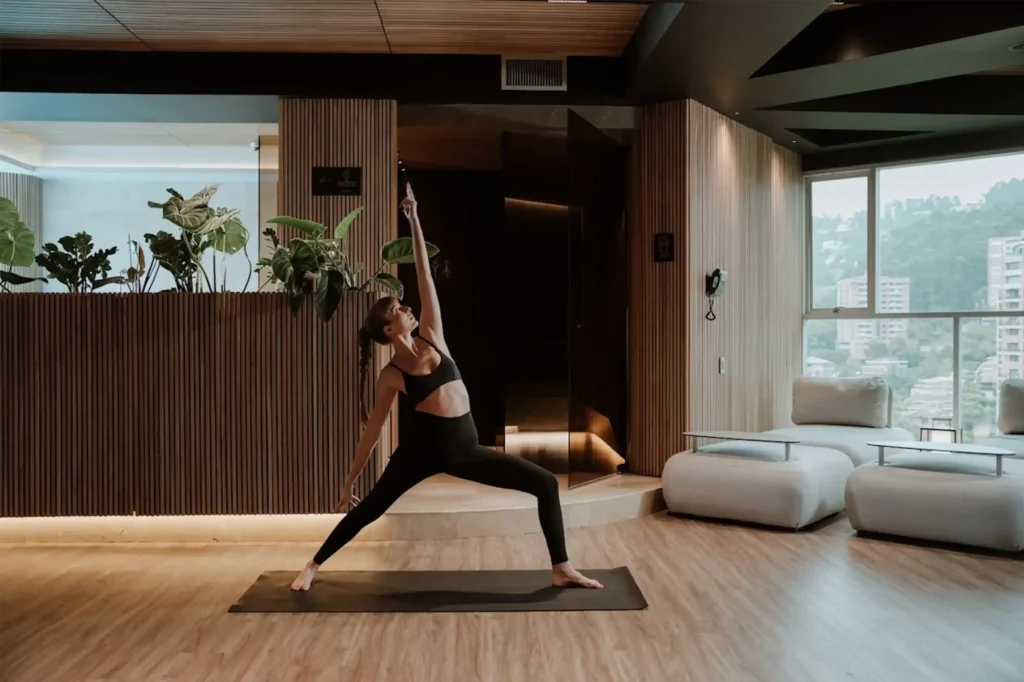Mujer practicando yoga en el salón de yoga de BINN Hotel boutique en Medellín con vistas a la montaña, plantas naturales y diseño moderno para su wellness.