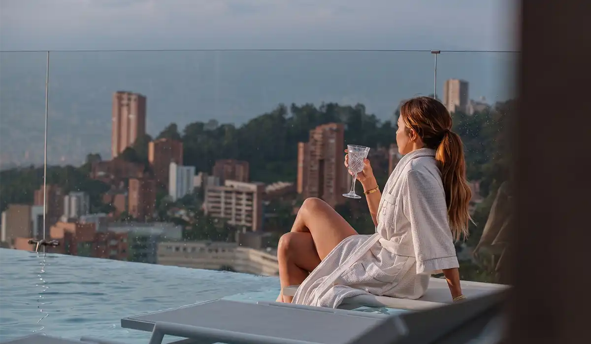 Mujer en bata BINN con copa junto a piscina infinita y vista al skyline de Medellín, experiencia Día de las Madres.