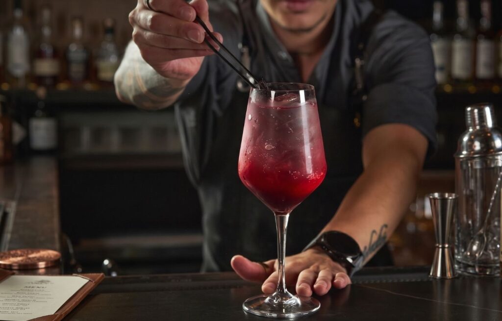 Bartender decorando un cóctel artesanal rojo en copa de cristal, reflejando la coctelería de lujo en Medellín.