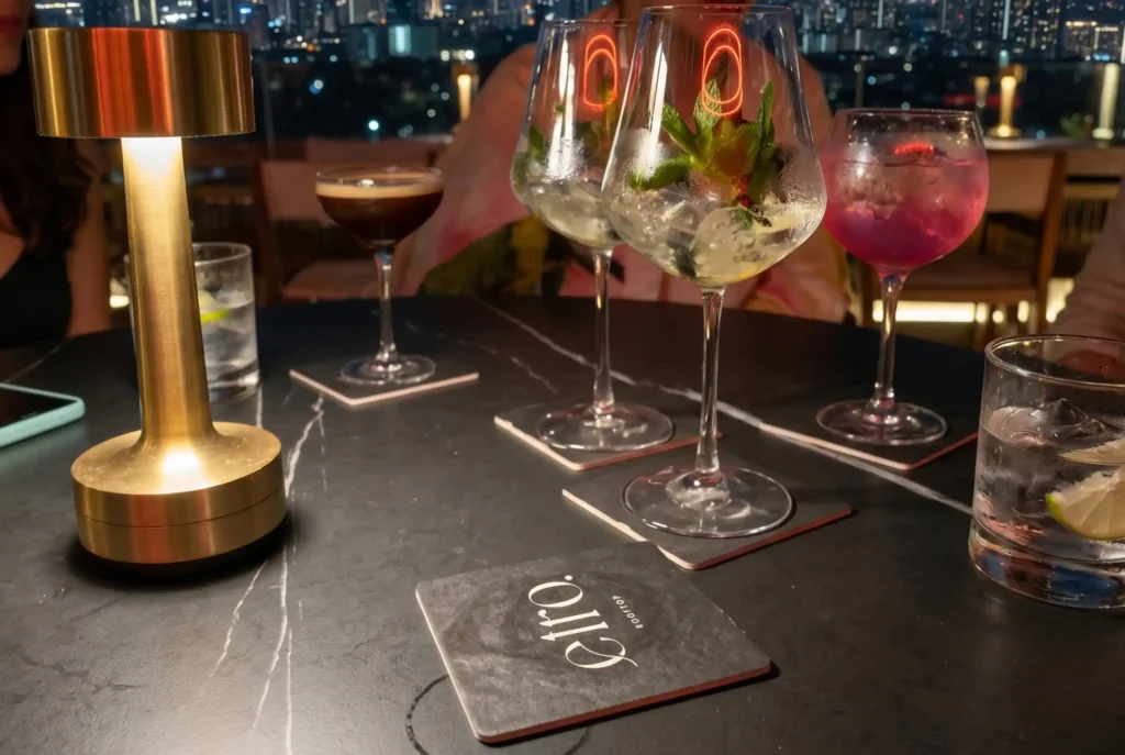 Mesa con cuatro cócteles y posavasos de ETRO Rooftop, bar de BINN Hotel con vista nocturna a Medellín en puente de mayo.

