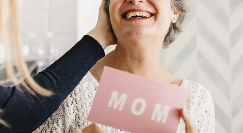 Mujer mayor sonriendo al recibir una tarjeta rosa de regalo día de la madre de su hija.