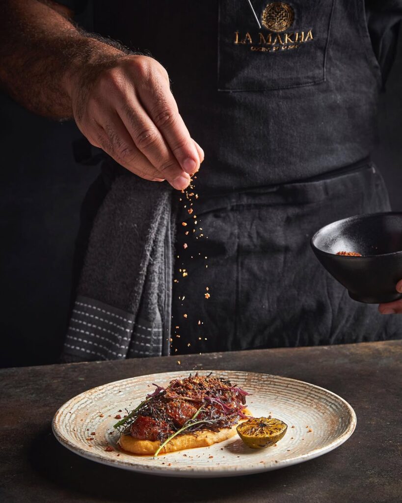 Chef de La Makha espolvoreando especias sobre chorizo artesanal con puré de arepa de mote y quesito crocante.