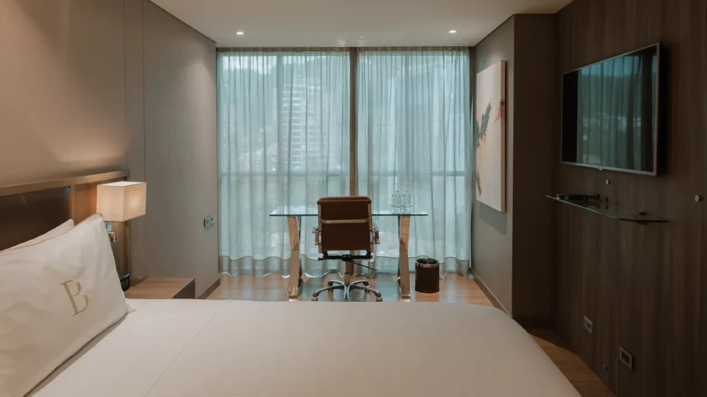BINN Hotel room with glass desk facing floor-to-ceiling window and king bed with B monogram.