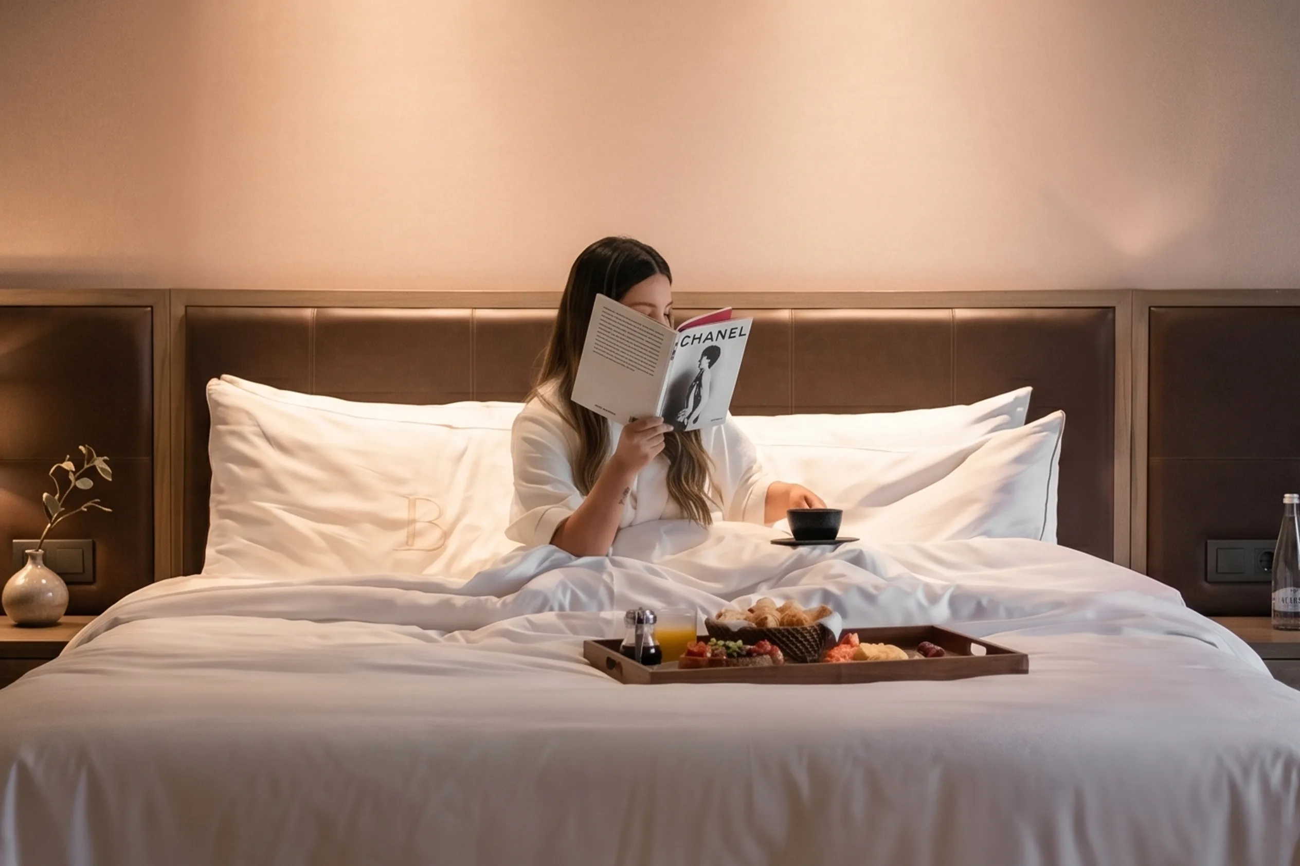 Persona leyendo en cama de BINN Hotel con bandeja de desayuno y ropa de cama blanca.