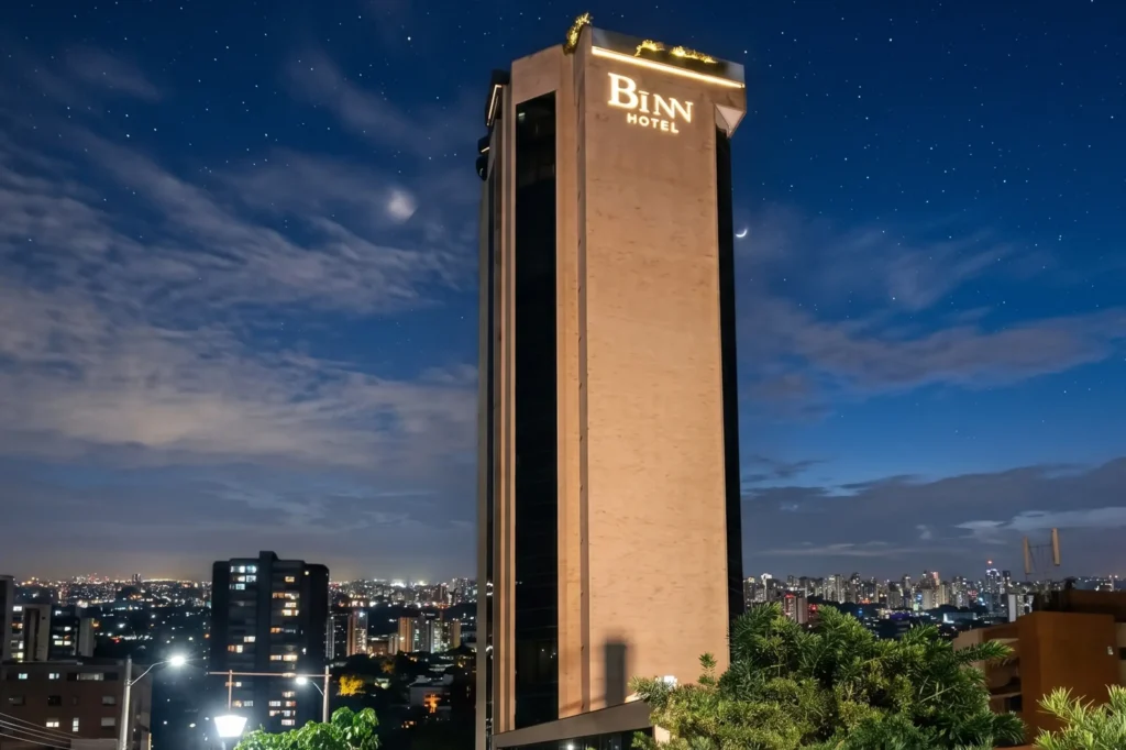 Torre de BINN Hotel iluminada de noche con el skyline de Medellin y cielo estrellado de fondo.