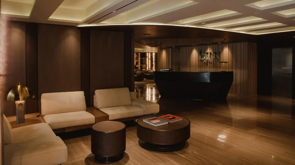 BINN Hotel reception lobby with curved dark counter, beige sofas and polished wood flooring.