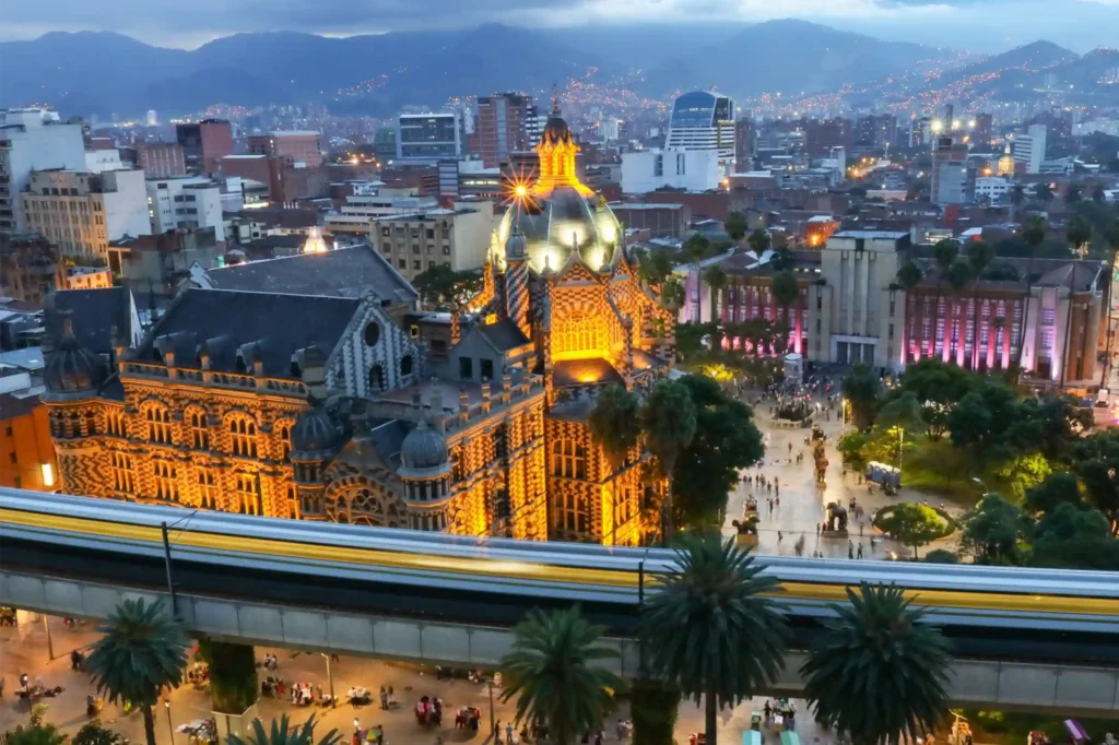 Aerial night view of Medellín Palace of Culture lit in gold with metro and Botero Plaza below.
