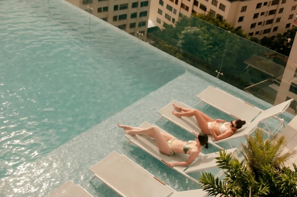 Dos personas tomando sol en sillas al borde de la piscina infinity del rooftop de BINN Hotel