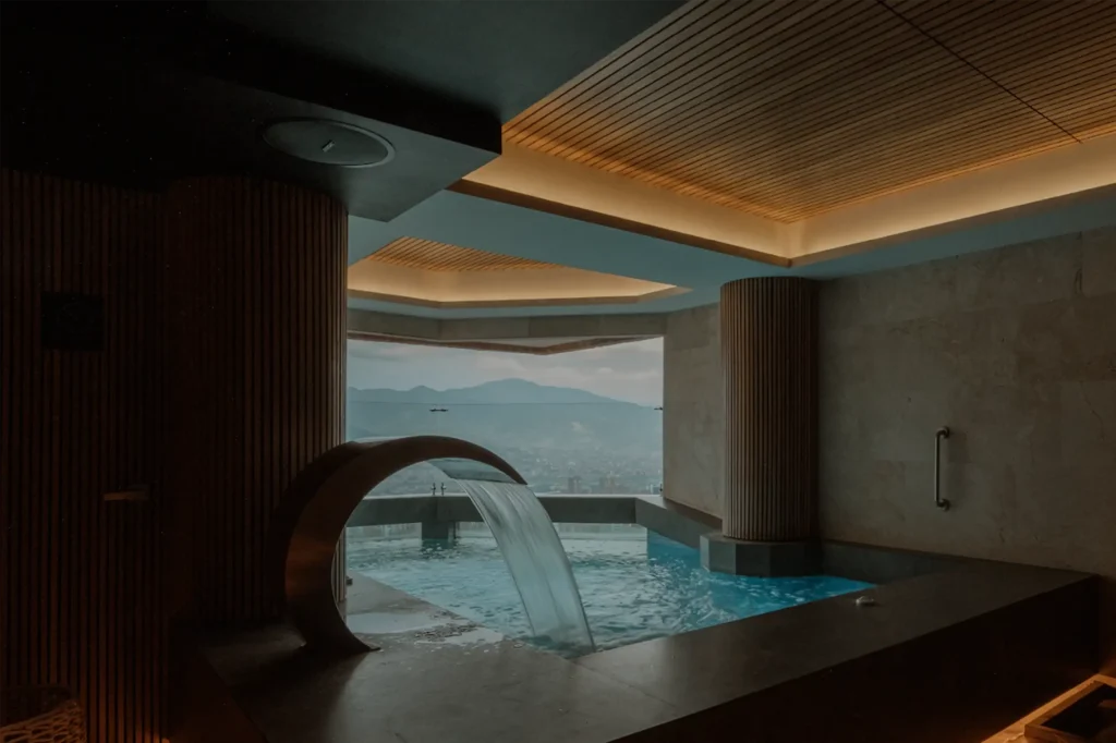 Piscina interior del spa de BINN Hotel con cascada en arco y vista panoramica a Medellin