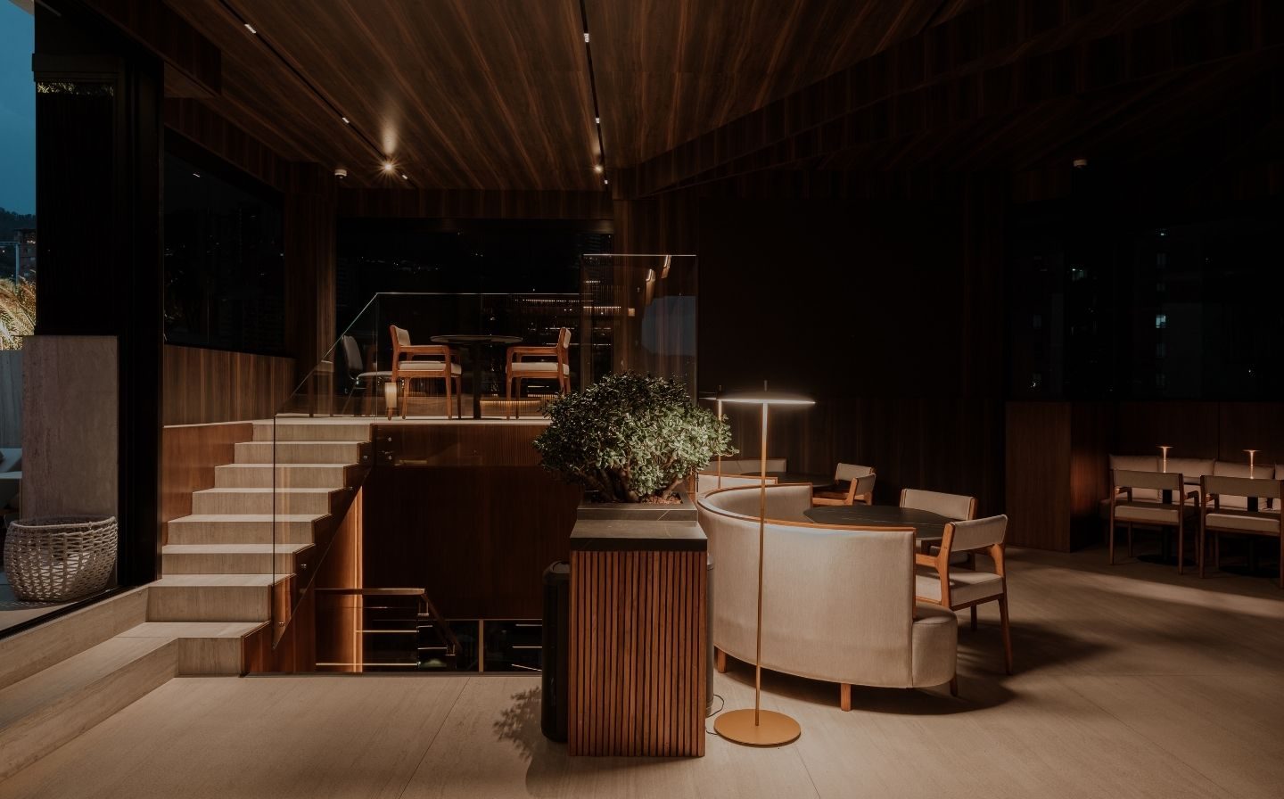 Arquitectura interior de dos niveles en Etro Rooftop de Binn Hotel con escalera de madera y sillones de noche.