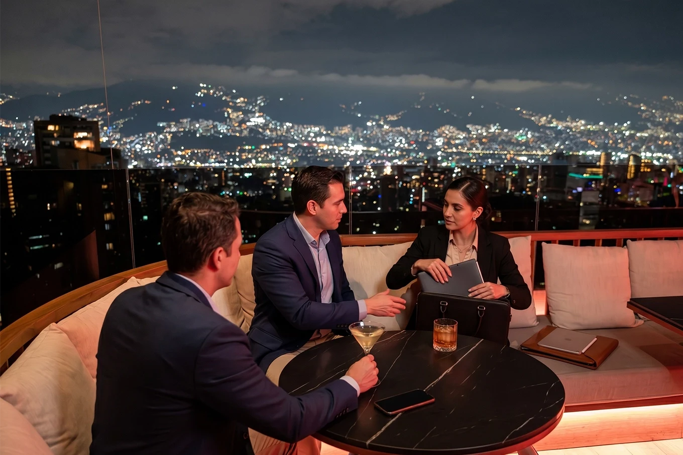 Tres profesionales en reunión afterwork en Etro Rooftop de Binn Hotel con skyline nocturno de Medellín.