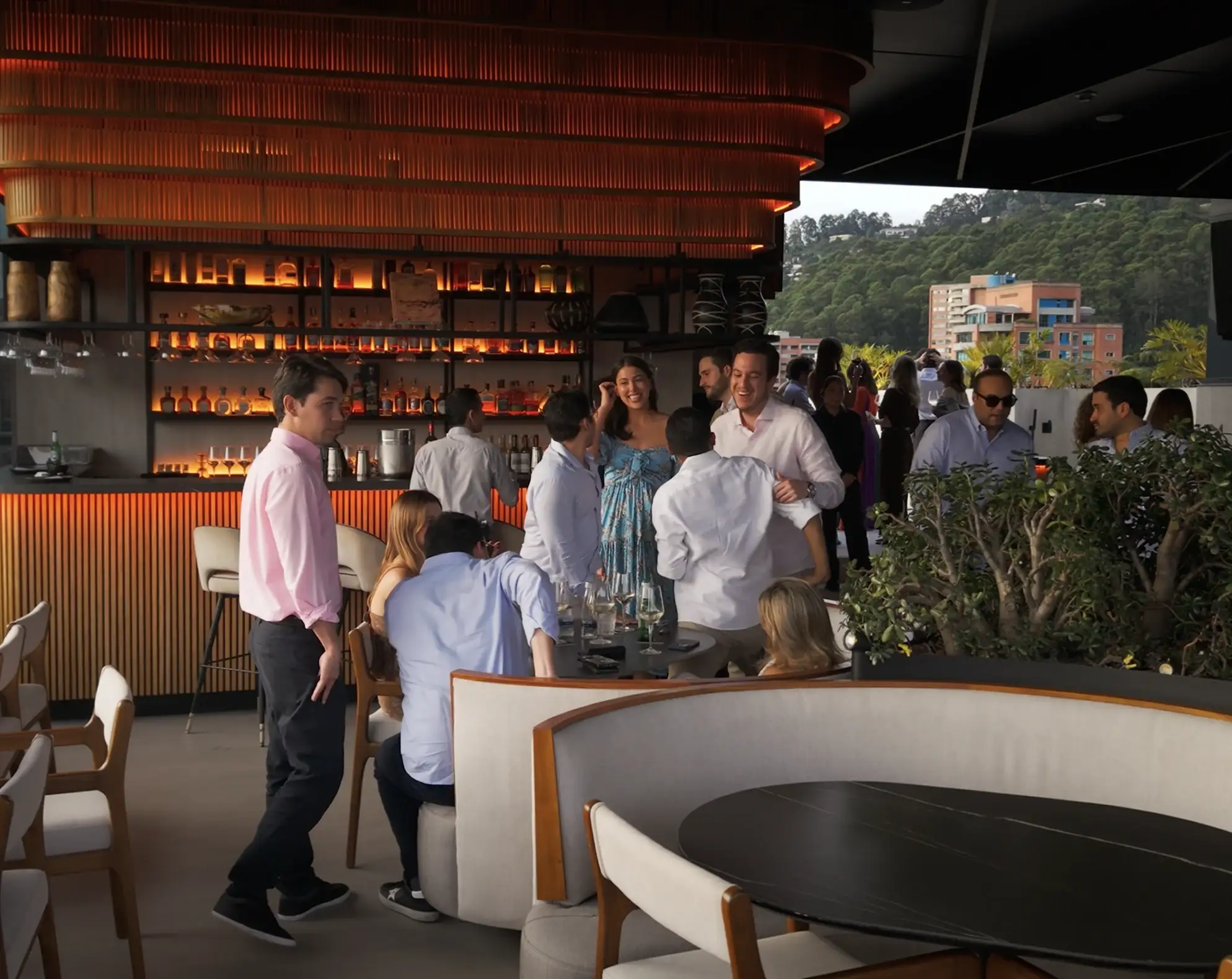 Grupo conversando en Etro Rooftop de Binn Hotel con barra iluminada y vegetación de El Poblado al fondo