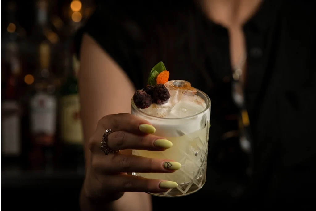 Hand holding a craft cocktail with berries and foam in a crystal glass at Etro Rooftop Medellín.