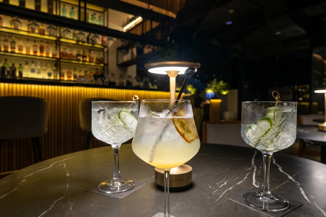 Tres cócteles en copas de cristal sobre mesa de mármol en Etro Rooftop de Binn Hotel