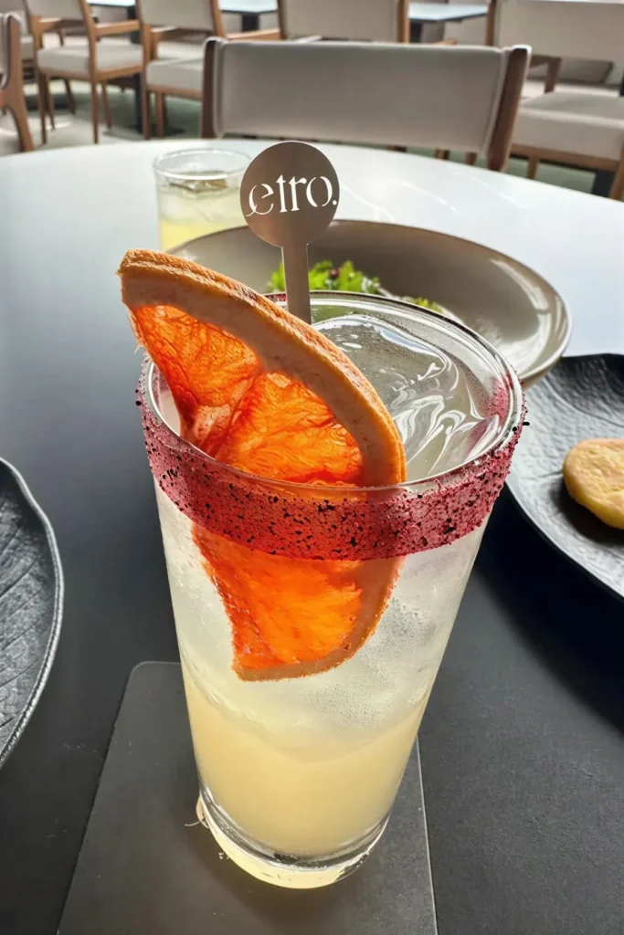 Etro Rooftop signature cocktail with dried orange garnish and branded stirrer on daytime terrace table.