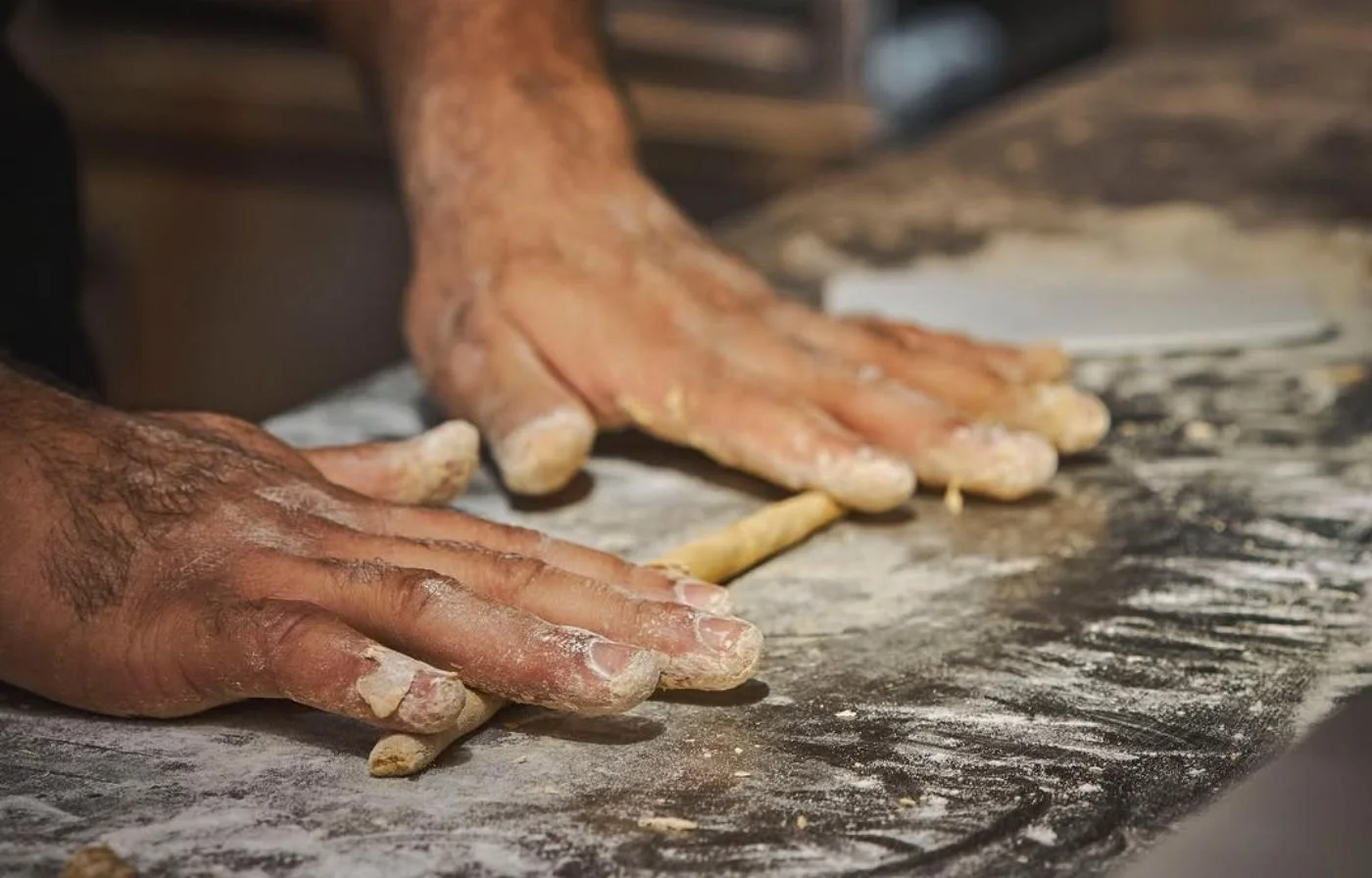 Manos formando tiras de masa fermentada sobre mesón enharinado en La Makha, Medellín