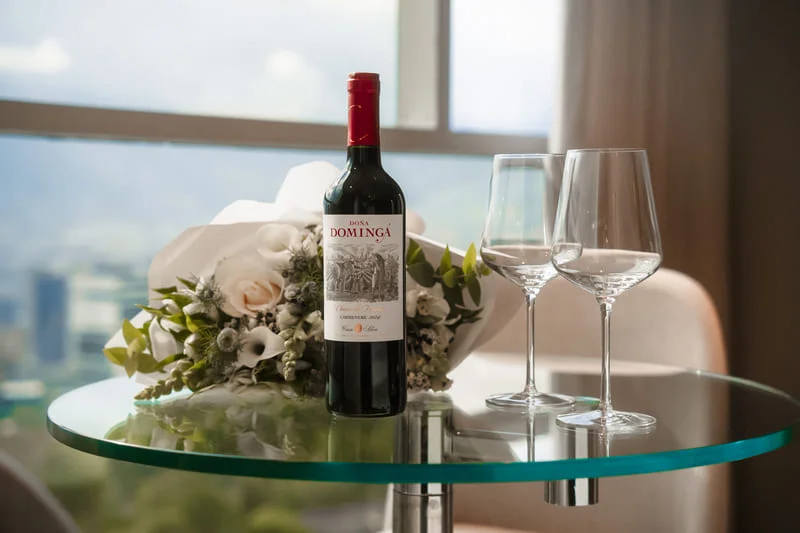 Red wine bottle and crystal glasses on glass table with Medellín city view through window.