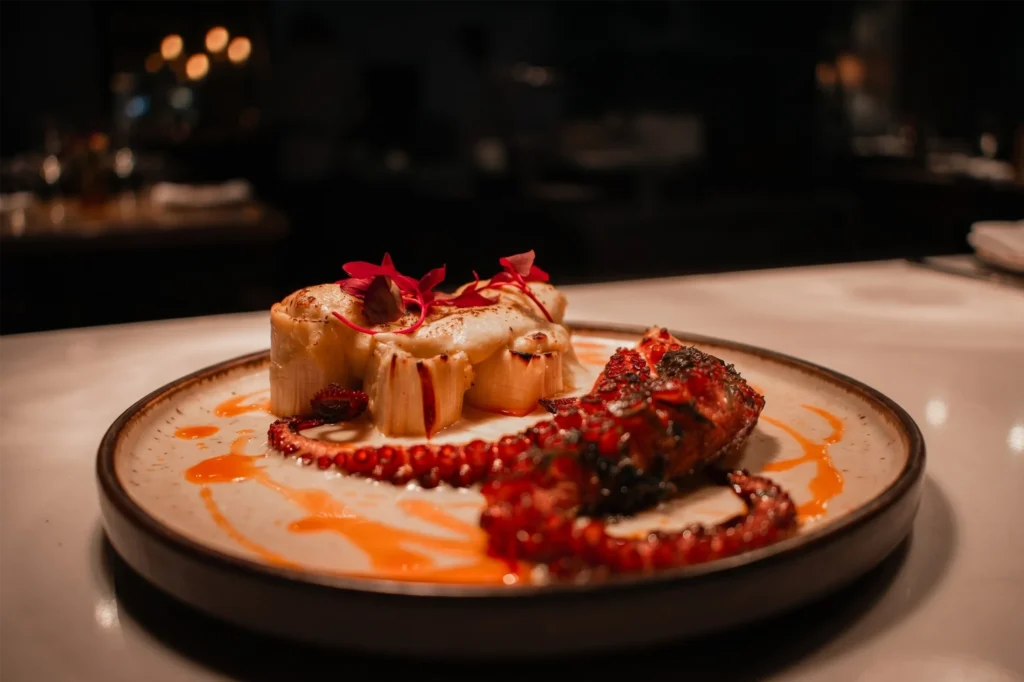 Pulpo a la brasa con salsa naranja y flores rojas en restaurante La Makha de BINN Hotel