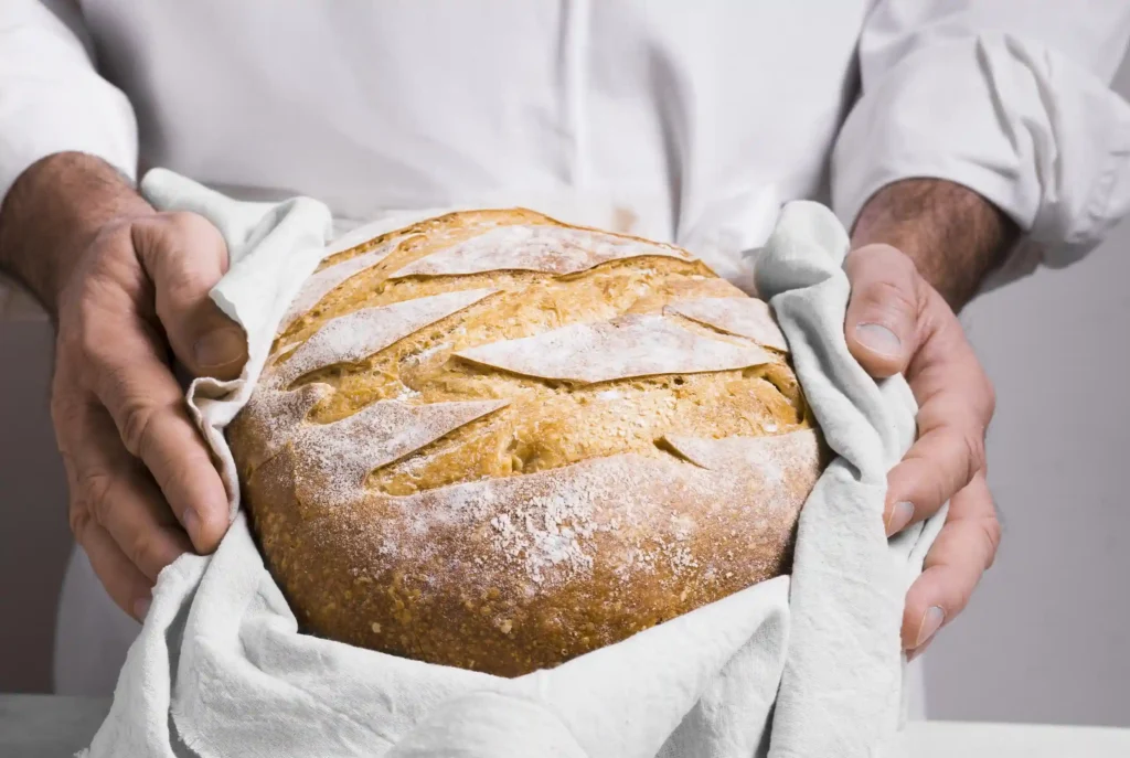 Chef sosteniendo hogaza de pan de masa madre con trigos ancestrales en La Makha, Medellín