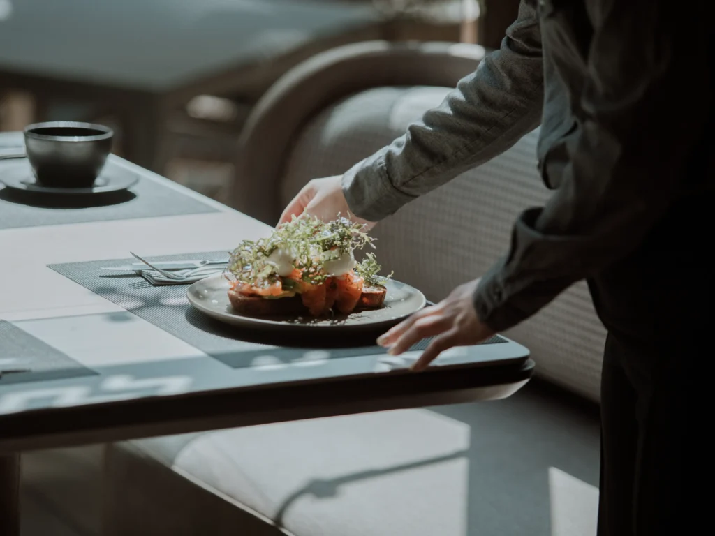 Mesero sirviendo tostada de salmón con huevo pochado y microgreens en La Makha, Medellín