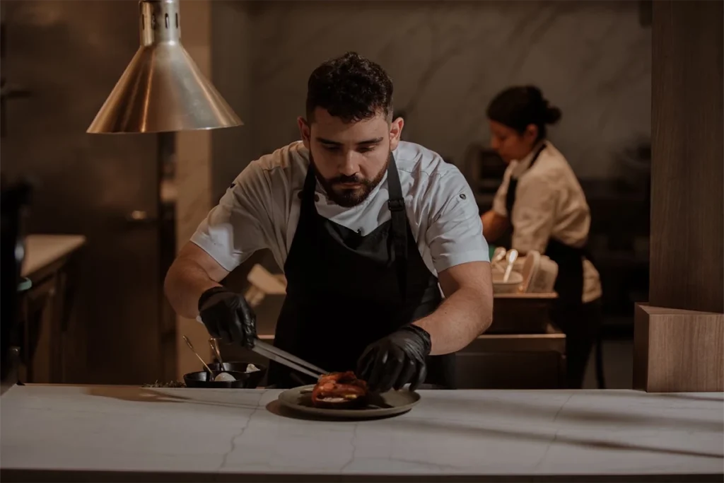 Chef at La Makha plating a dish in the restaurant's open kitchen in Medellín