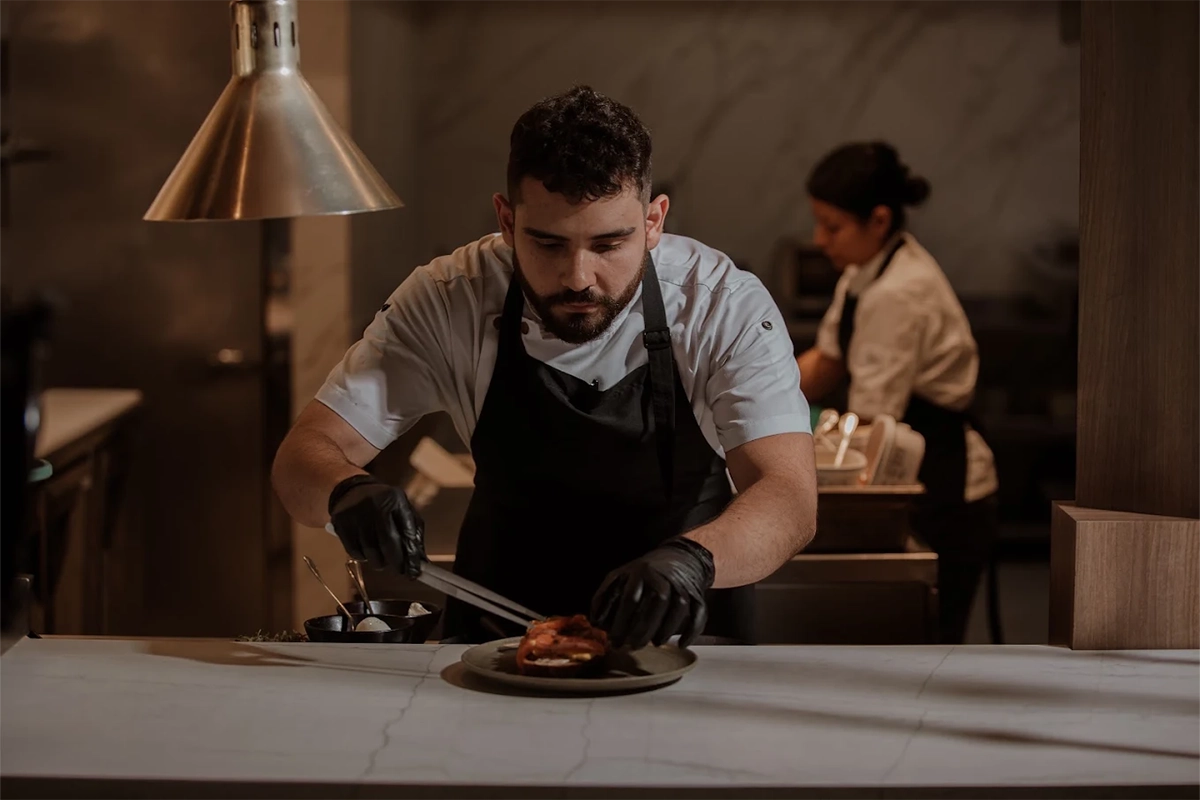 Chef at La Makha plating a dish in the restaurant's open kitchen in Medellín