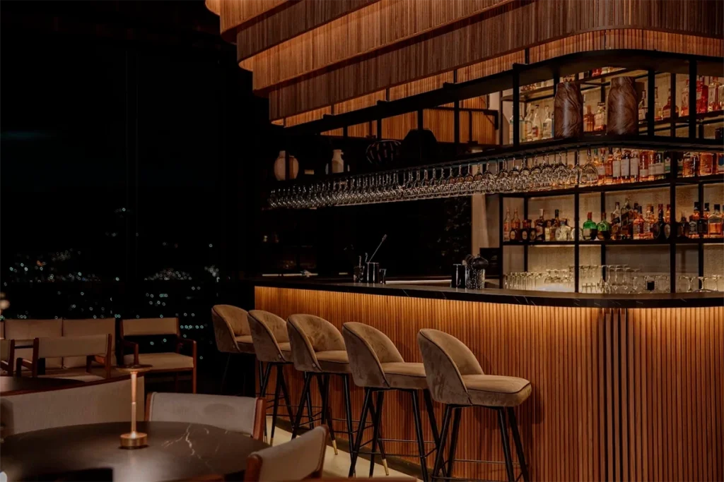 Etro Rooftop's warm wooden bar lit up at night overlooking Medellin's city lights.
