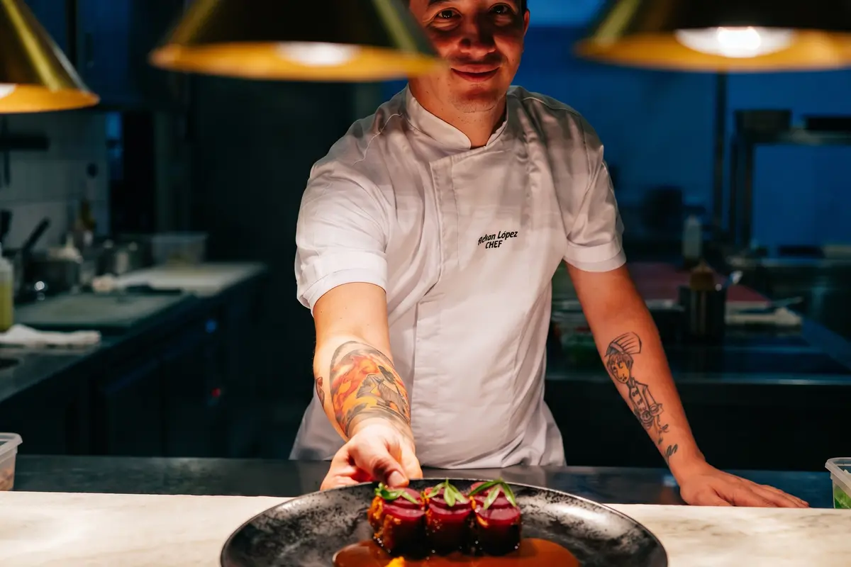 Chef at La Makha restaurant in Medellín presenting a signature gourmet dish at the pass.