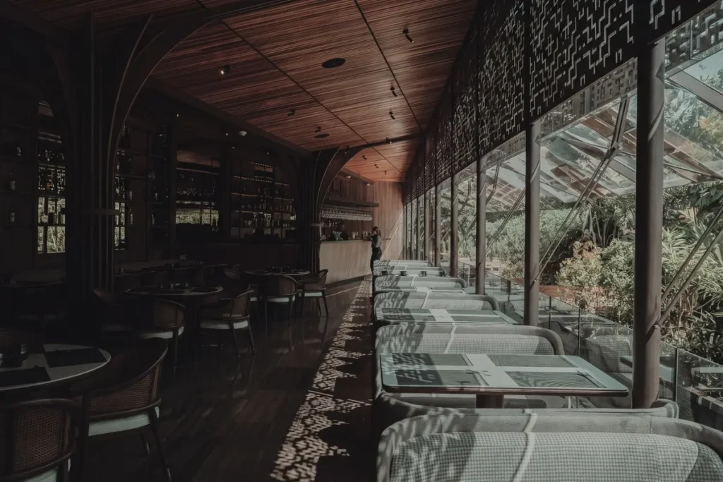 Dimly lit dining room at La Makha restaurant in Medellín with floor-to-ceiling windows and a cocktail bar in the background.