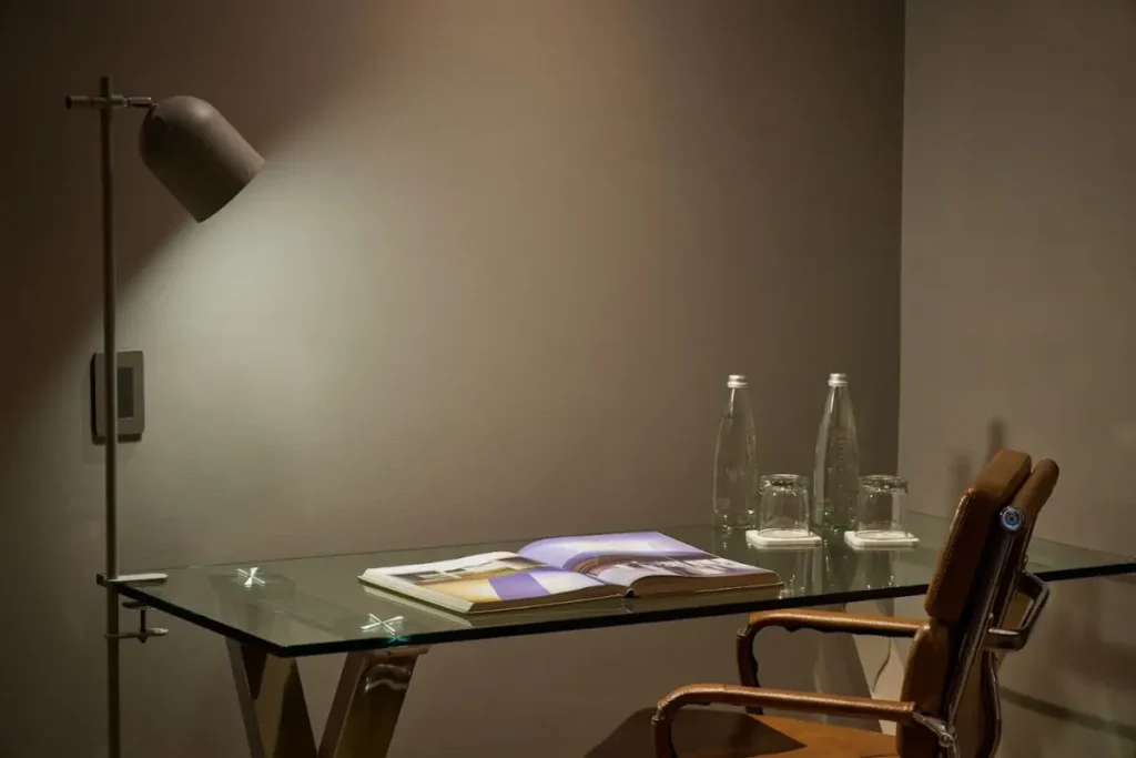 Escritorio de cristal con lámpara moderna, silla de cuero y botellas de agua en la Habitación Superior Twin de Binn Hotel Medellín