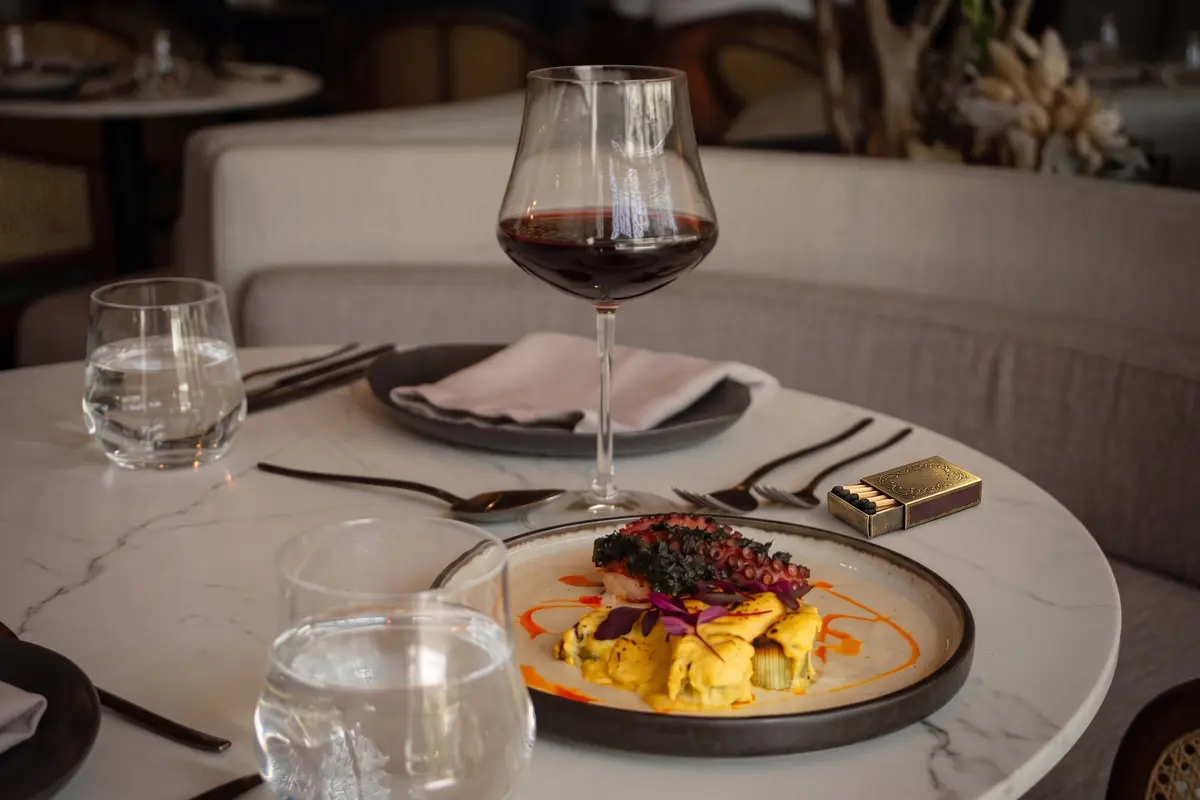 Gourmet grilled octopus dish on yellow sauce served with a glass of red wine on a marble table at La Makha restaurant in Medellín.