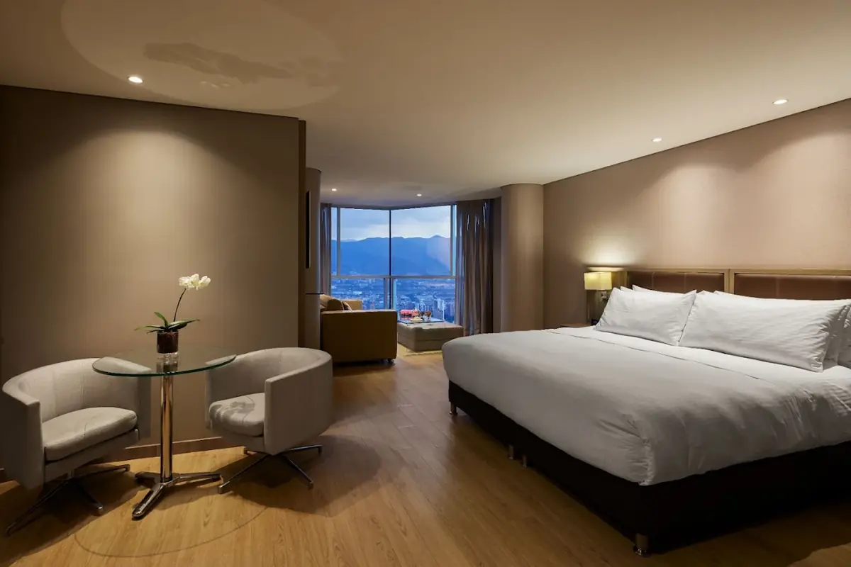 Habitación Superior King en Binn Hotel Medellín con cama king size, mesa de cristal con dos sillas y ventanal con vista panorámica a la ciudad