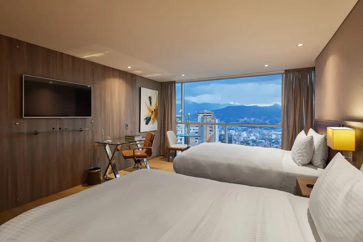 Escritorio de cristal con lámpara moderna, silla de cuero y botellas de agua en la Habitación Superior Twin de Binn Hotel Medellín