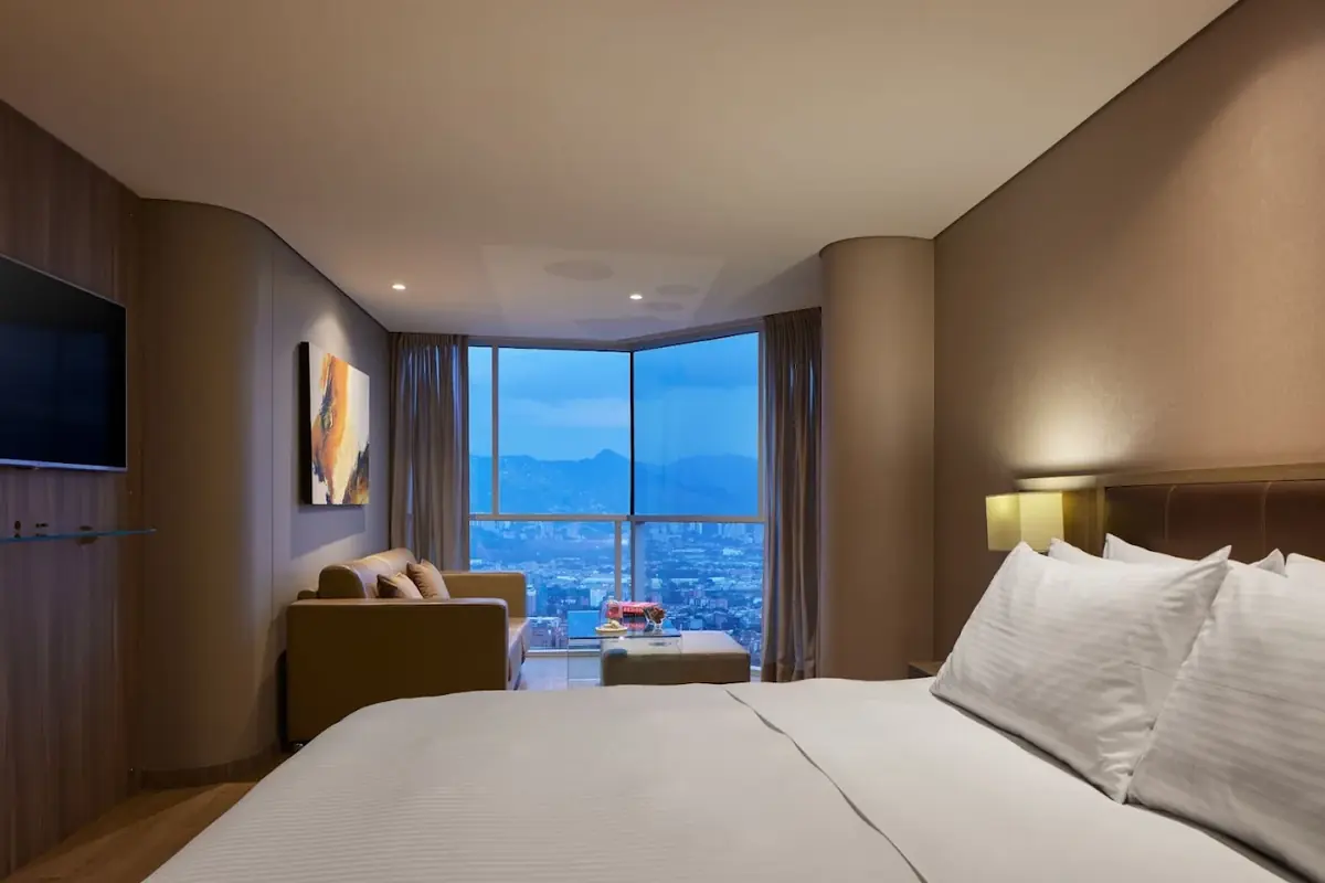Junior Suite Deluxe en Binn Hotel Medellín con cama de lujo, zona de estar con sofá y grandes ventanales con vista a la ciudad