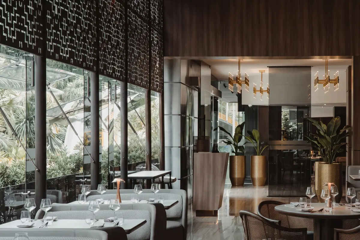 Dining area of La Makha restaurant in El Poblado featuring set tables, gold chandeliers, and large glass windows.