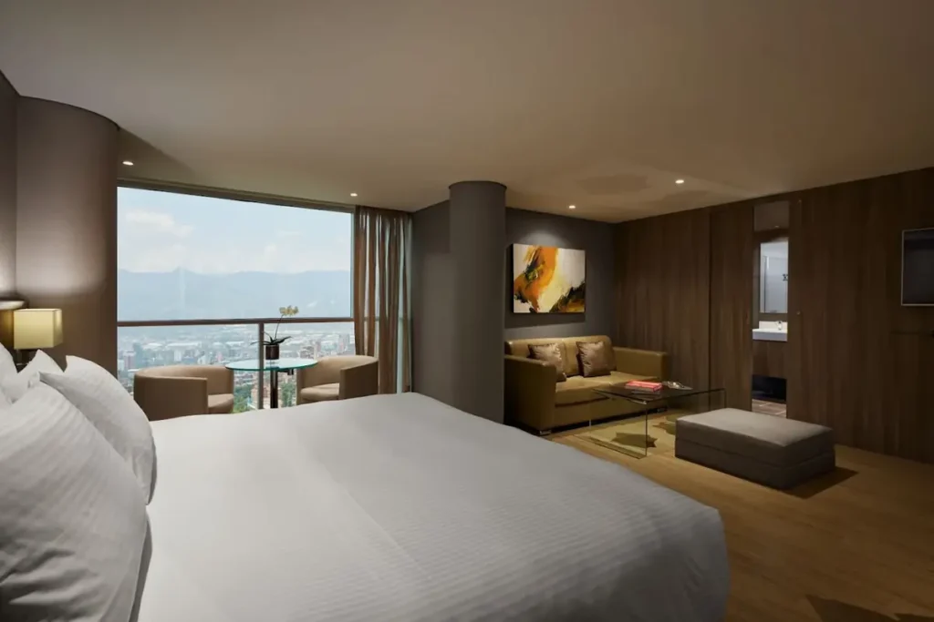 Luxury suite at Binn Hotel Medellin featuring a king bed, living area with sofa, and large windows with panoramic views
