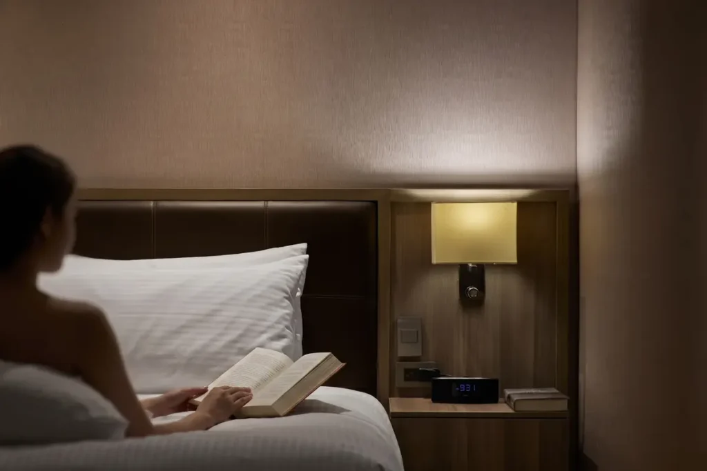 Mujer recostada leyendo un libro en la cama de una habitación en Binn Hotel Medellín junto a una lámpara de noche