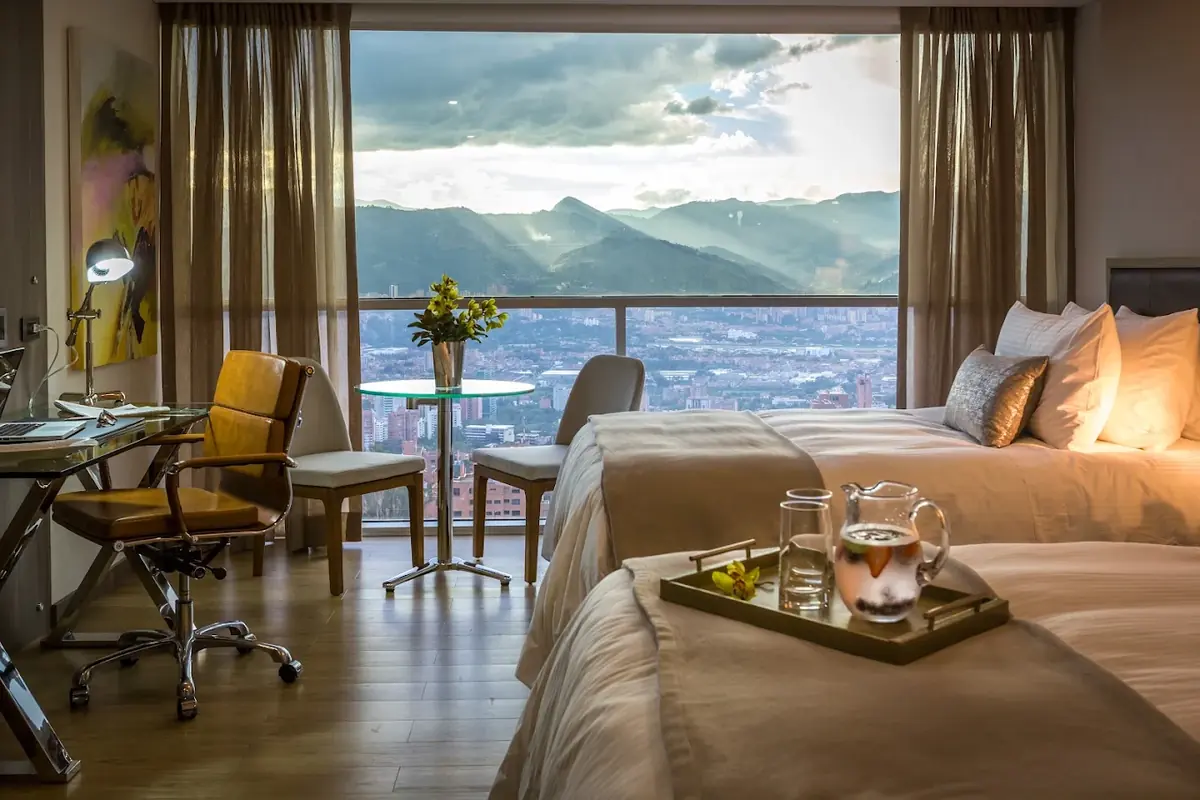 Double room at Binn Hotel Medellin featuring a desk, two beds, and floor-to-ceiling window overlooking the city and mountains