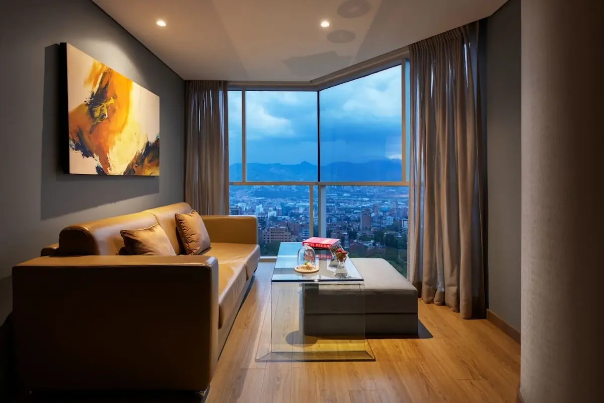 Living room area in a suite at Binn Hotel Medellin featuring a leather sofa, glass coffee table, and large window with city view