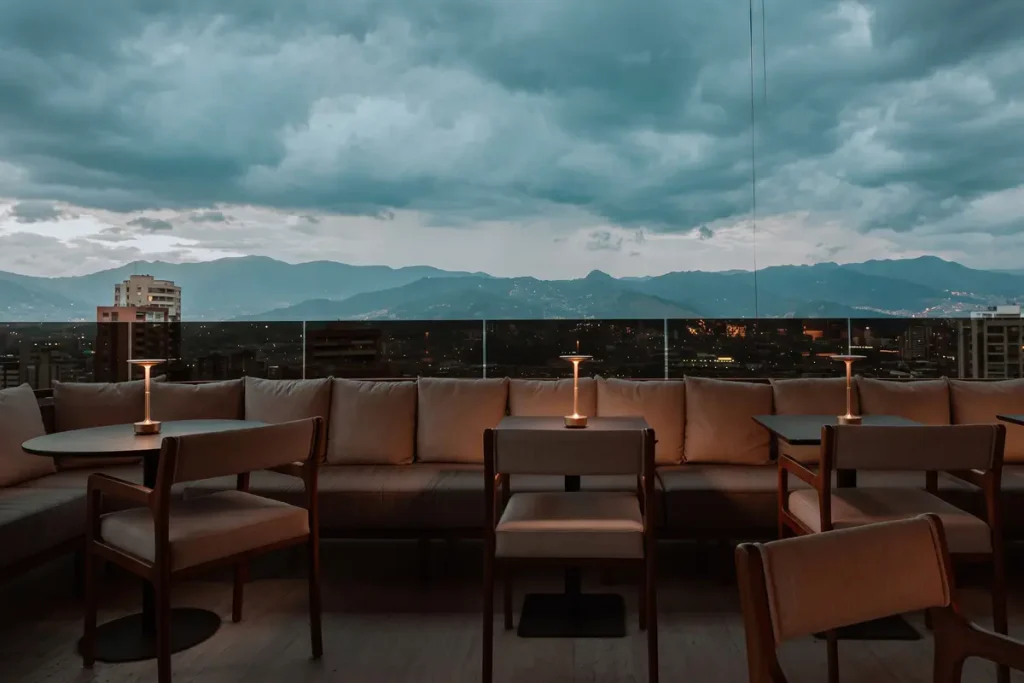 Mesas en la terraza al aire libre de Etro Rooftop Medellín con vista panorámica a las montañas bajo el cielo al atardecer.