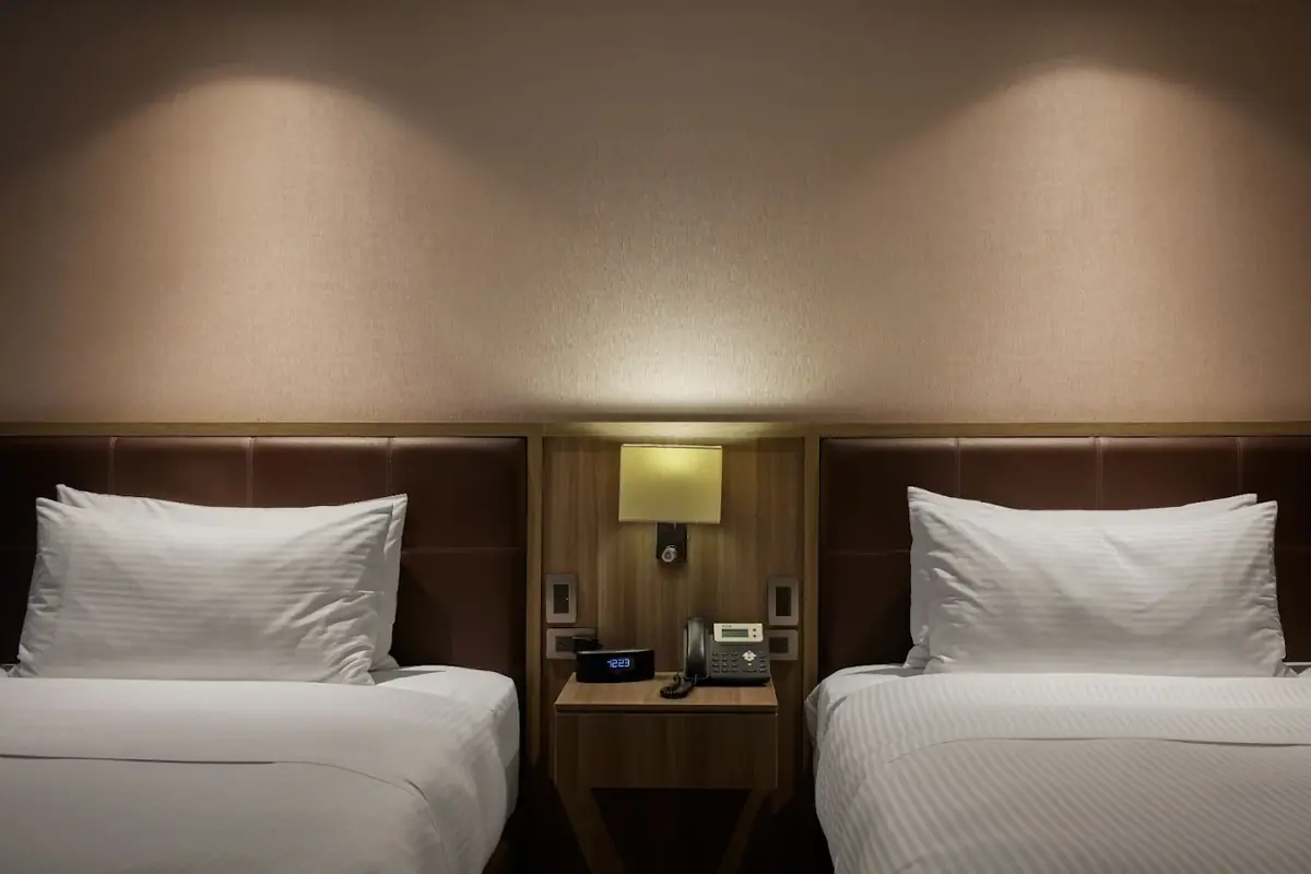Two twin beds with crisp white linens and an illuminated nightstand in a room at Binn Hotel Medellin