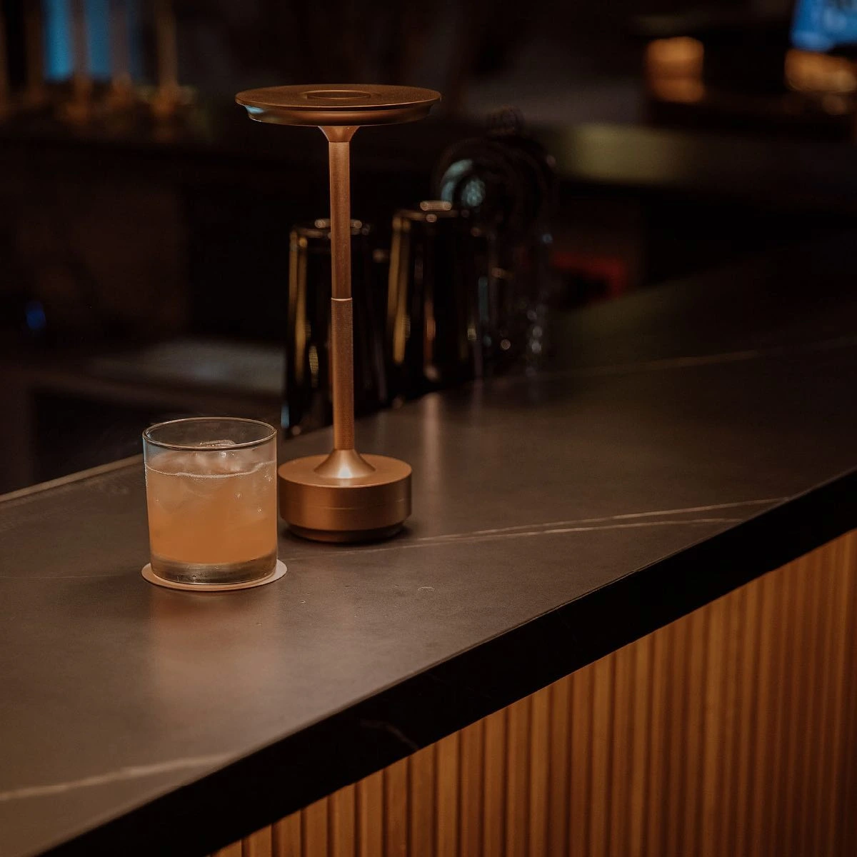 Vaso de cóctel artesanal servido junto a una lámpara dorada en la barra de Etro Rooftop para la temporada de lluvias.