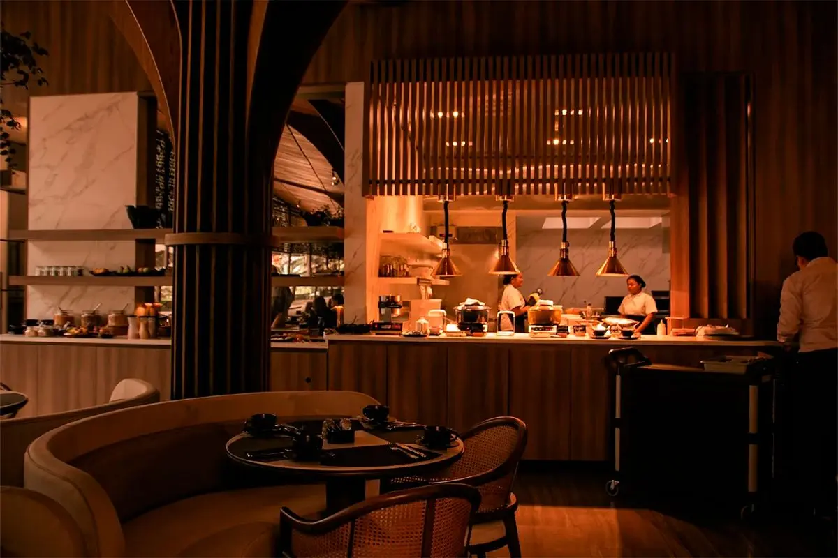 Group dinner area at La Makha restaurant featuring a view of the warm-lit open kitchen and dining tables.