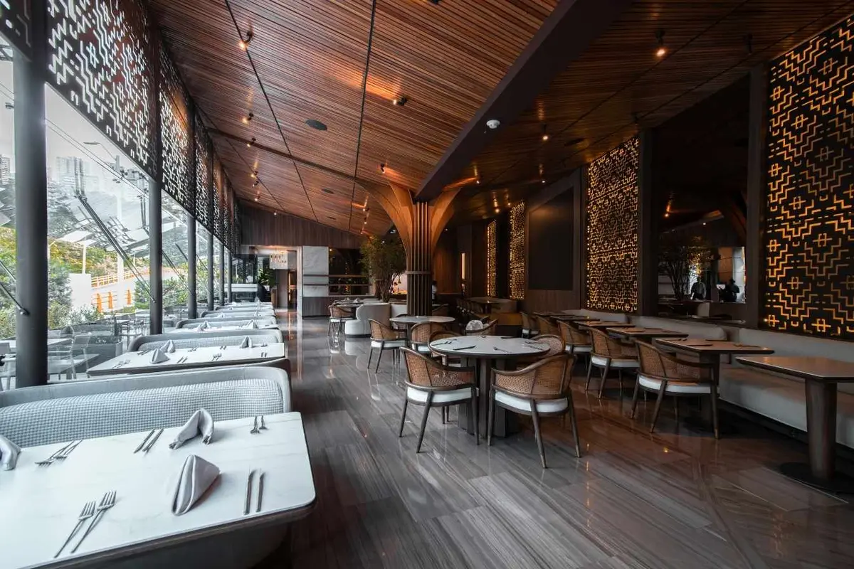 Salón interior del restaurante La Makha en Medellín con mesas dispuestas, sillas de madera y diseño arquitectónico moderno.