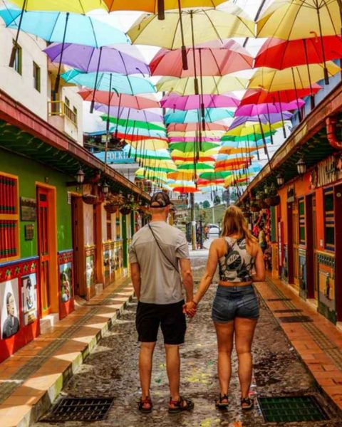 Pareja de la mano caminando por un colorido callejón con paraguas, en un destino premium cerca de Medellín