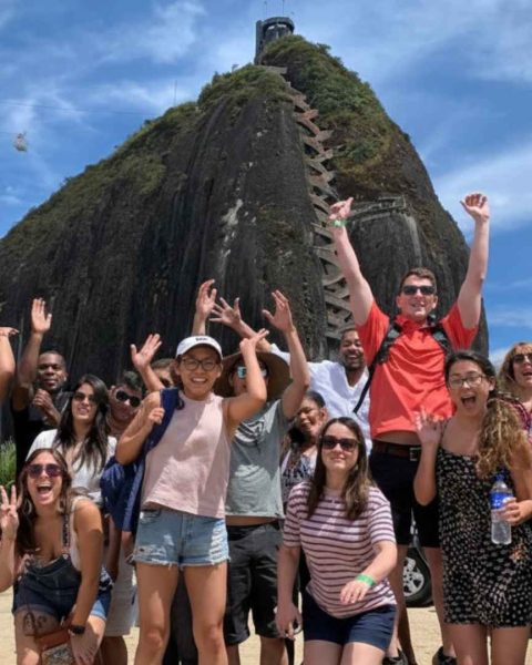 Grupo de personas sonriendo frente a una majestuosa montaña guatape en Antioquia, disfrutando de una experiencia de lujo
