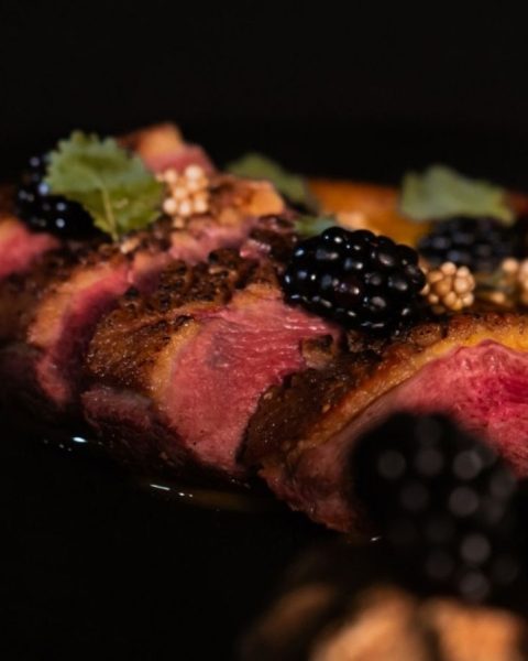 Un plato negro con carne, moras y nueces, representando la fusión de arte local y gastronomía en La Makha